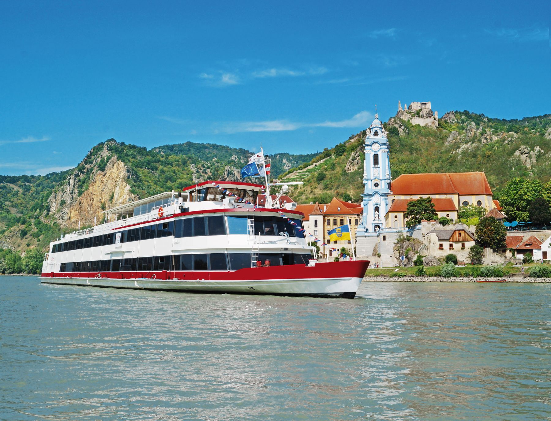 Ein Schiff der DDSG Blue Danube Schifffahrt GmbH fährt auf der Donau, im Hintergrund ist Dürnstein zu sehen.