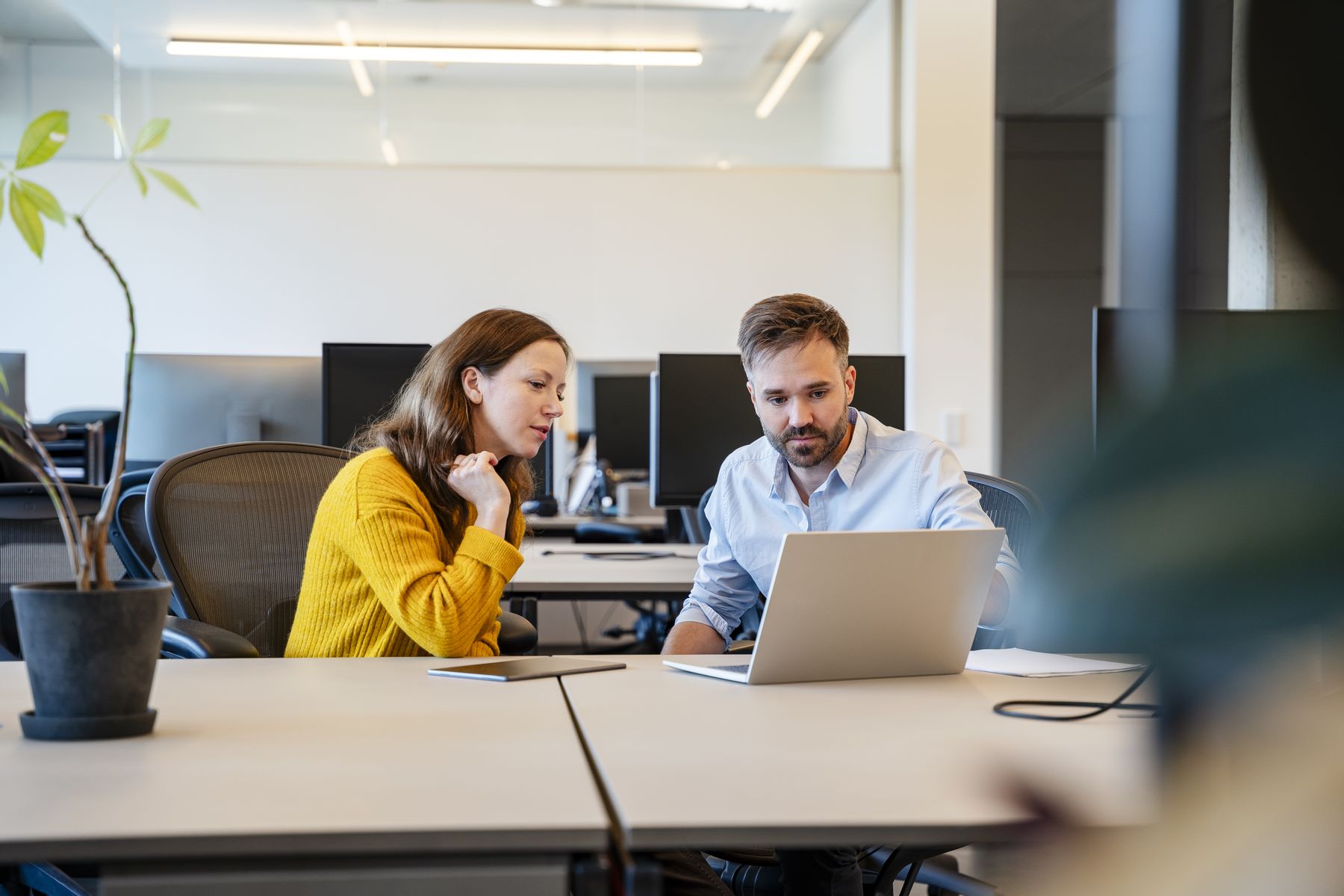 Mann und Frau arbeiten gemeinsam an einem Laptop in einem modernen Büro.