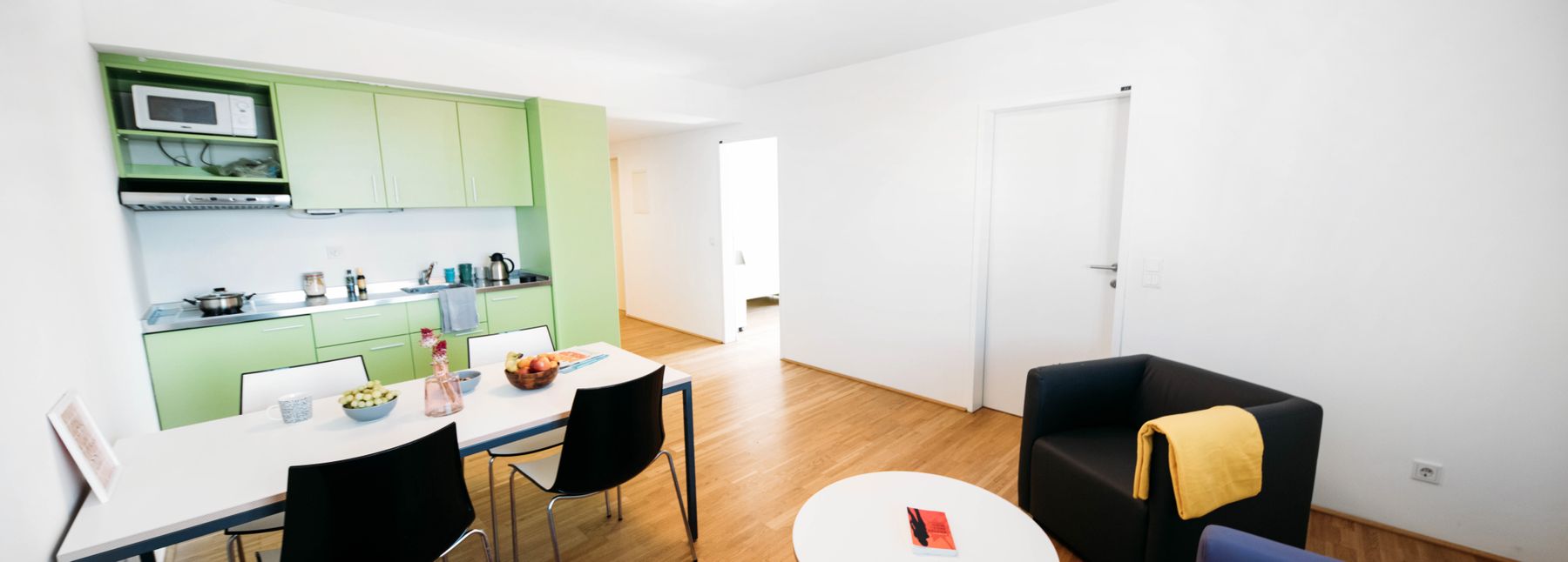 Wohnung der Viennabase mit einer kleinen grünen Küchenzeile, einem Tisch und drei bequemen Stühlen.