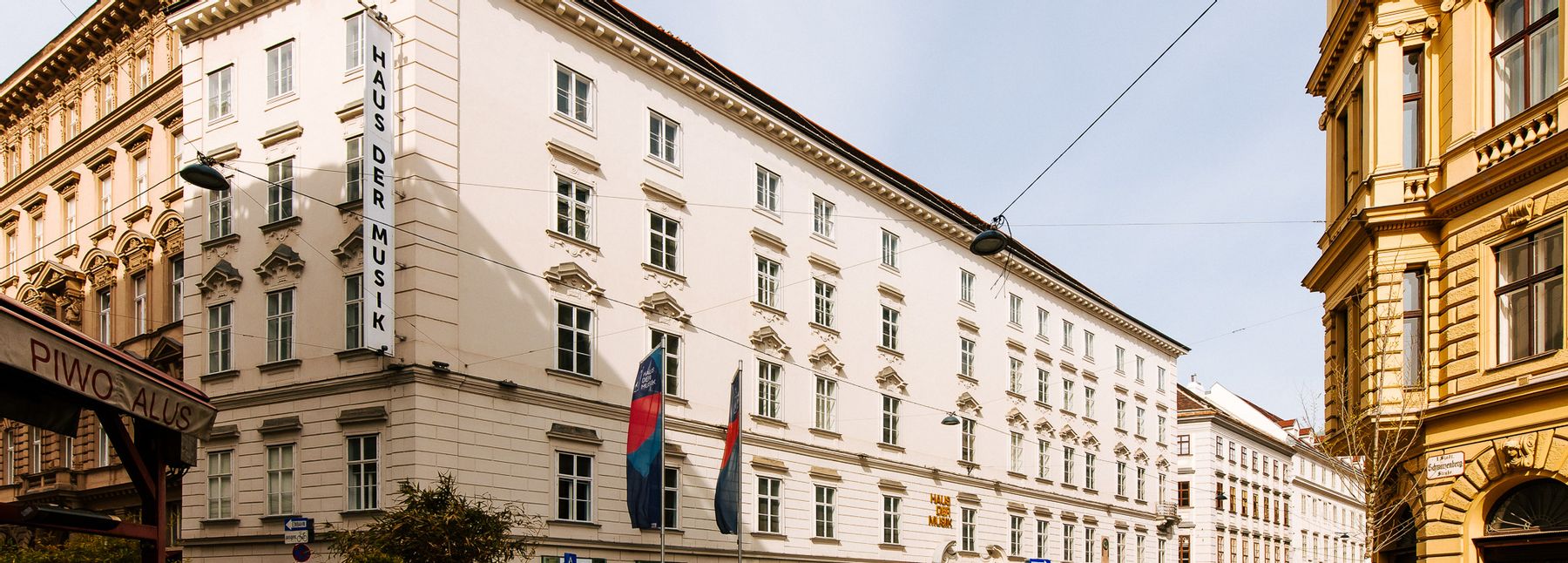 Zu sehen ist das Haus der Musik mit wehenden Fahnen vor dem Eingangsbereich.