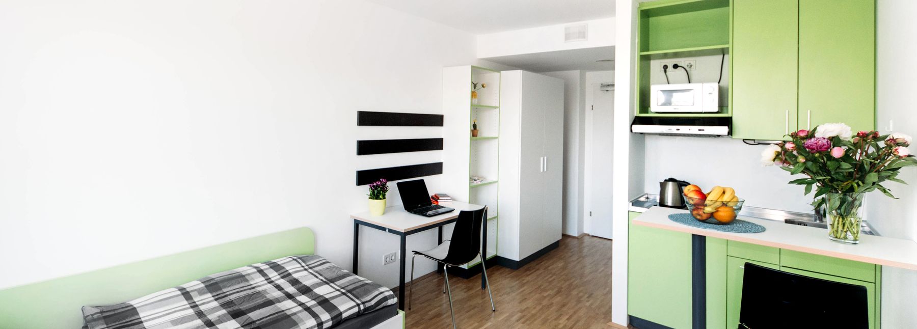 Wohnung der Viennabase mit einer kleinen grünen Küchenzeile, einem Bett und einem Schreibtisch.