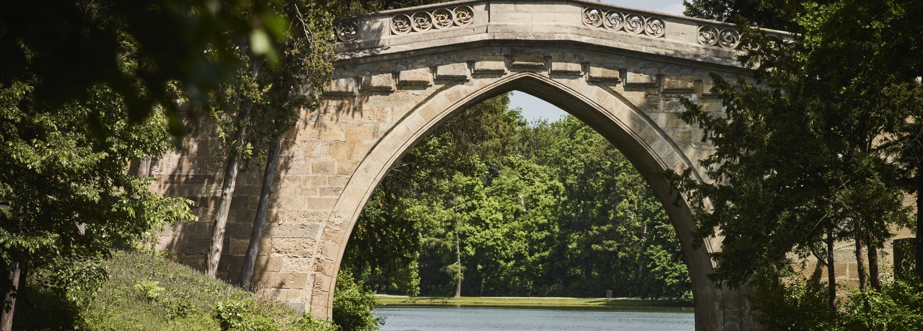 Eine Brücke aus Stein über einen See im Schlosspark Laxenburg.