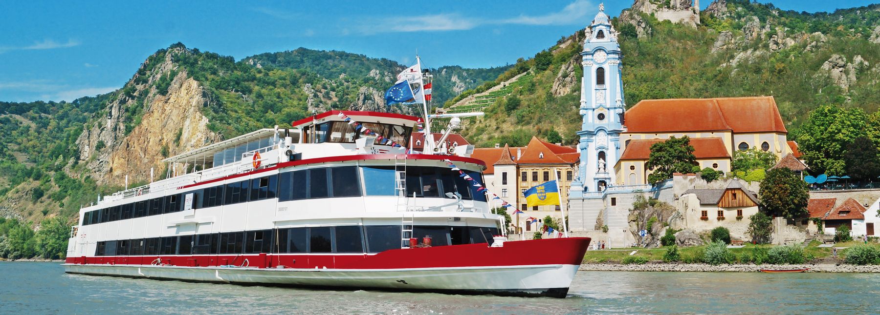 Ein Schiff der DDSG Blue Danube Schifffahrt GmbH fährt auf der Donau, im Hintergrund ist Dürnstein zu sehen.