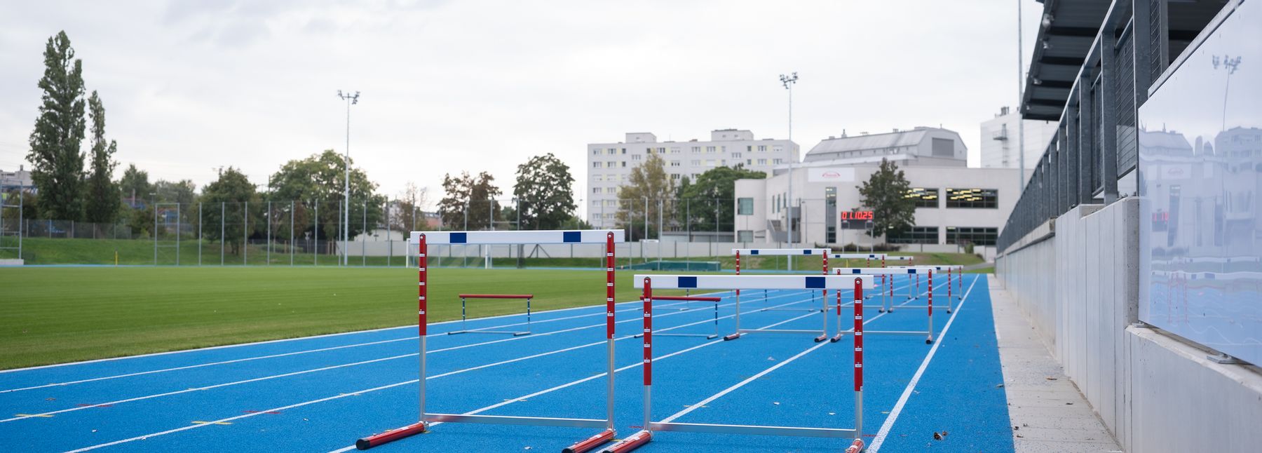 Blaue Laufbahn der Leichtathletikanlage mit aufgebauten Hürden, die restliche Anlage im Hintergrund.