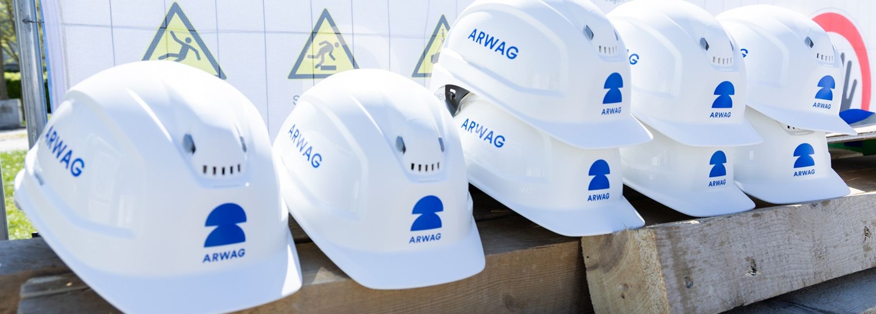 Eine Reihe weißer Bauhelme mit dem Arwag Logo ist zu sehen.