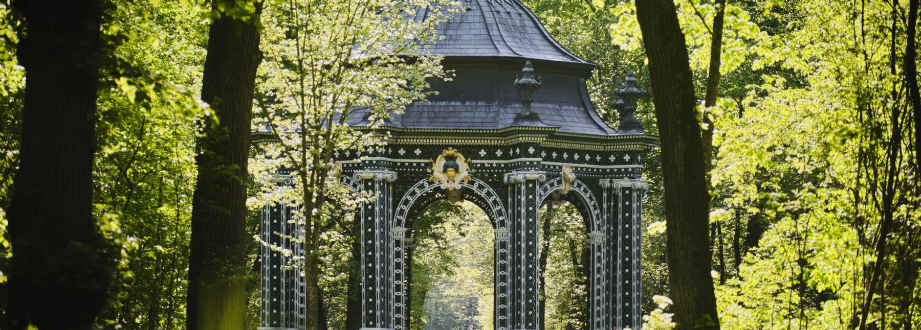 Der Pavillon im Schlosspark Laxenburg ist zwischen grünen Bäumen zu sehen.