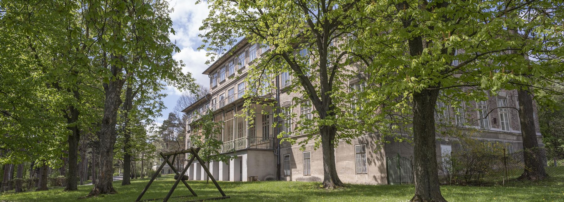 Steingebäude am Otto-Wagner-Areal; im Vordergrund eine Wiese mit einer Holzschaukel und Bäumen.