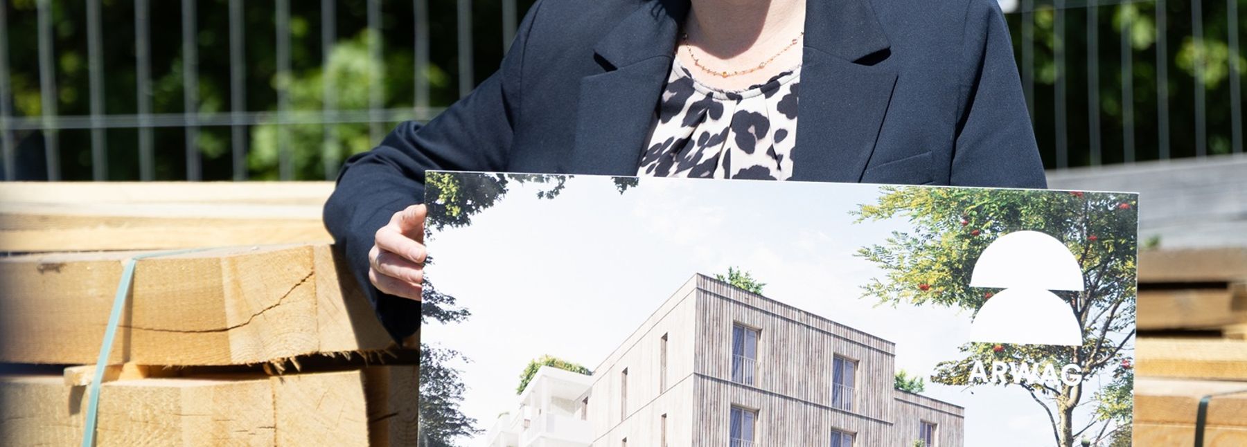 Die Wohnbaustadträtin ist mit einer Tafel, auf der die Visualisierung des Baus zu sehen ist, abgebildet.