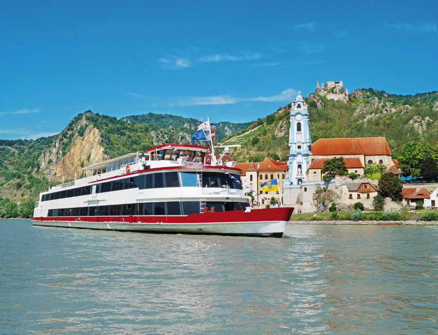 Ein Schiff der DDSG Blue Danube Schifffahrt GmbH fährt auf der Donau, im Hintergrund ist Dürnstein zu sehen.
