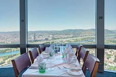 Gedeckter Tisch im Turmrestaurant des Donauturms in Wien mit weißer Tischwäsche, Gläsern und Servietten sowie Panoramablick über die Donau und die Wiener Stadtlandschaft.