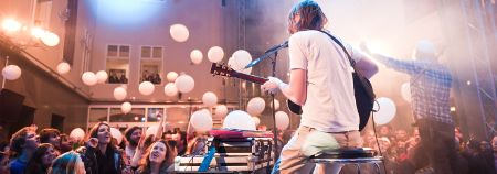 Sänger mit Gitarre auf Bühne, davor das jubelnde Publikum, weiße Luftballons schweben in der Luft