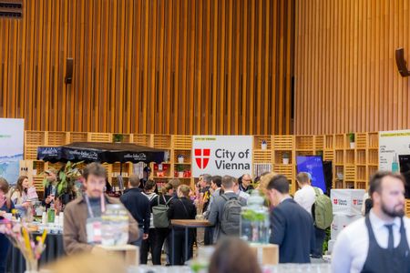 Eine Gruppe von Menschen bei einer Art Messe, im Hintergrund ein großer Aufsteller mit Logo der Stadt Wien auf Englisch