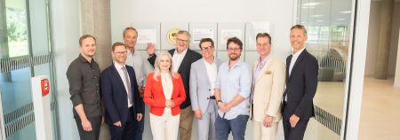 8 Herren und eine Dame stehen vor der klimaaktiv Gold Plakette