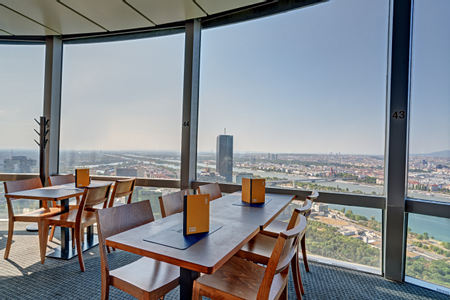 Innenansicht des Turmcafés im Donauturm in Wien mit Holztischen und großen Panoramafenstern mit Blick über die Wiener Skyline, die Donau und umliegende Grünflächen.