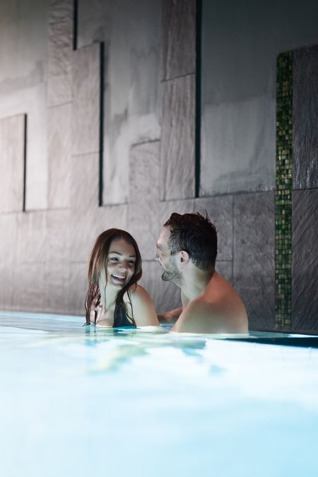 Innenbereich der Therme Wien: Ein Mann und eine Frau stehen im Wasser vor einer Steinwand.