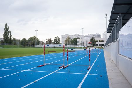 Blaue Laufbahn der Leichtathletikanlage mit aufgebauten Hürden, die restliche Anlage im Hintergrund.