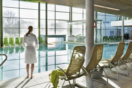 Eine Frau im Bademantel steht neben einem Pool.