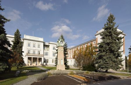 Direktionsgebäude am Otto-Wagner-Areal, weiß und teilweise aus Backstein; im Vordergrund eine Standuhr und Bäume.