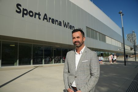Mann im grauen Sakko steht vor Sporthalle