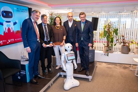 Vier Männer und eine Frau stehen hinter einem kleinen weißen Roboter