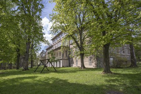Steingebäude am Otto-Wagner-Areal; im Vordergrund eine Wiese mit einer Holzschaukel und Bäumen.