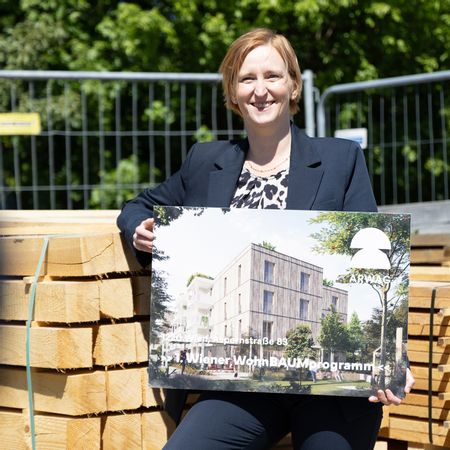 Die Wohnbaustadträtin ist mit einer Tafel, auf der die Visualisierung des Baus zu sehen ist, abgebildet.