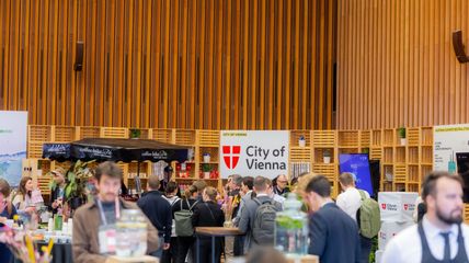 Eine Gruppe von Menschen bei einer Art Messe, im Hintergrund ein großer Aufsteller mit Logo der Stadt Wien auf Englisch