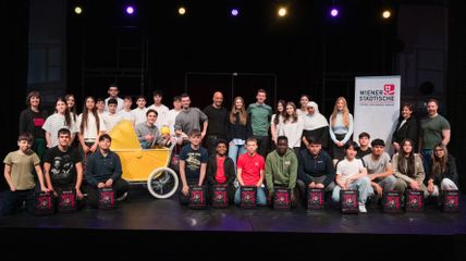 Zu sehen ist ein Gruppenfoto von Schüler*innen auf derBühne des Ronacher