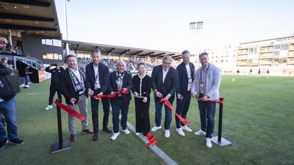 Eine Gruppe von Menschen steht auf einem Fußballfeld und schneidet gemeinsam ein rotes Band durch