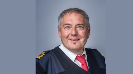 Zu sehen ist ein Porträtfoto von Johannes Kammerer in seiner dunkelblauen Kapitänsuniform mit roter Krawatte.