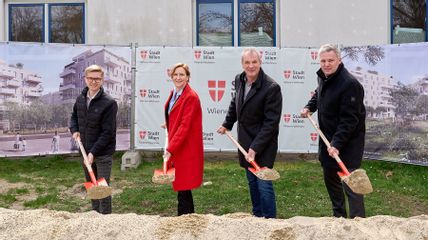 Drei Männer und eine Frau mit Schaufeln vor einem Sandhaufen